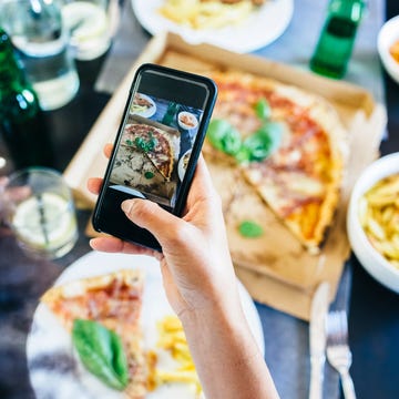 Hand taking cell phone picture of pizza on table Hand taking cell phone picture of pizza on table