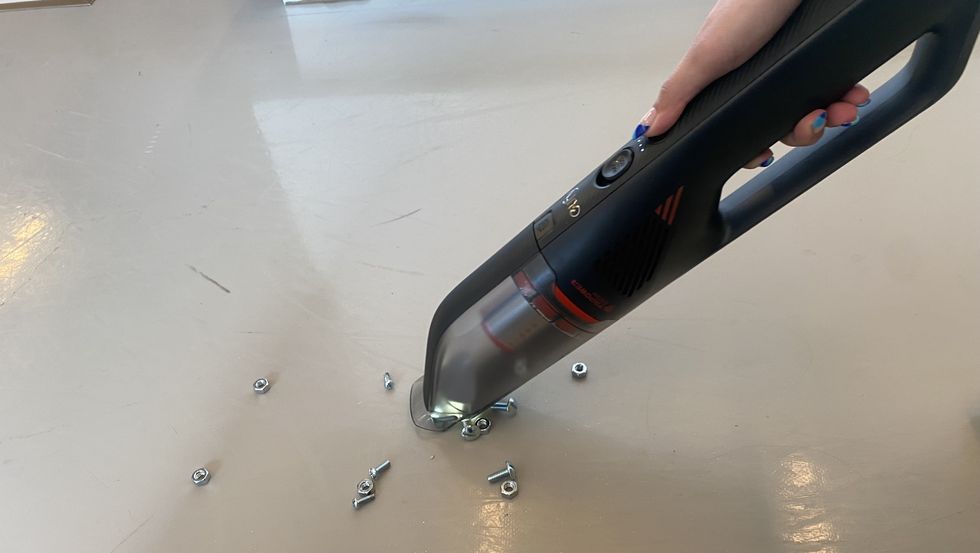 handheld vacuum picking up screws and nuts on bare floor