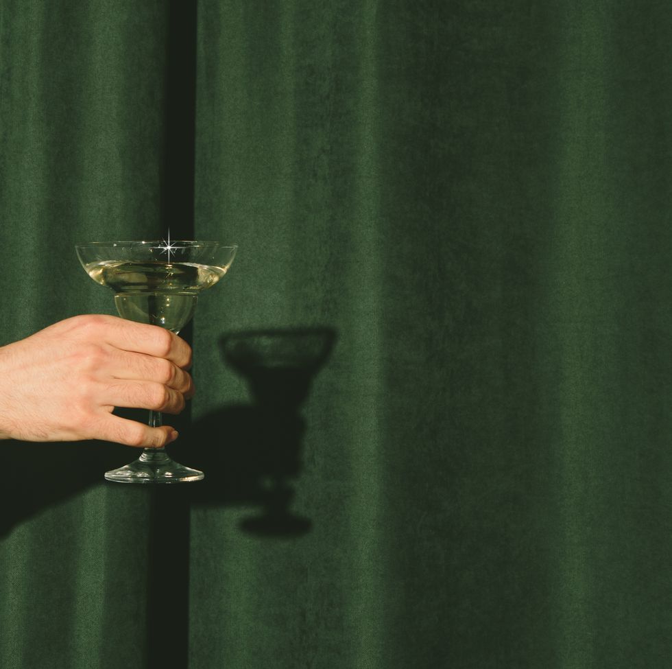 hand with a martini glass sticks out from the curtains