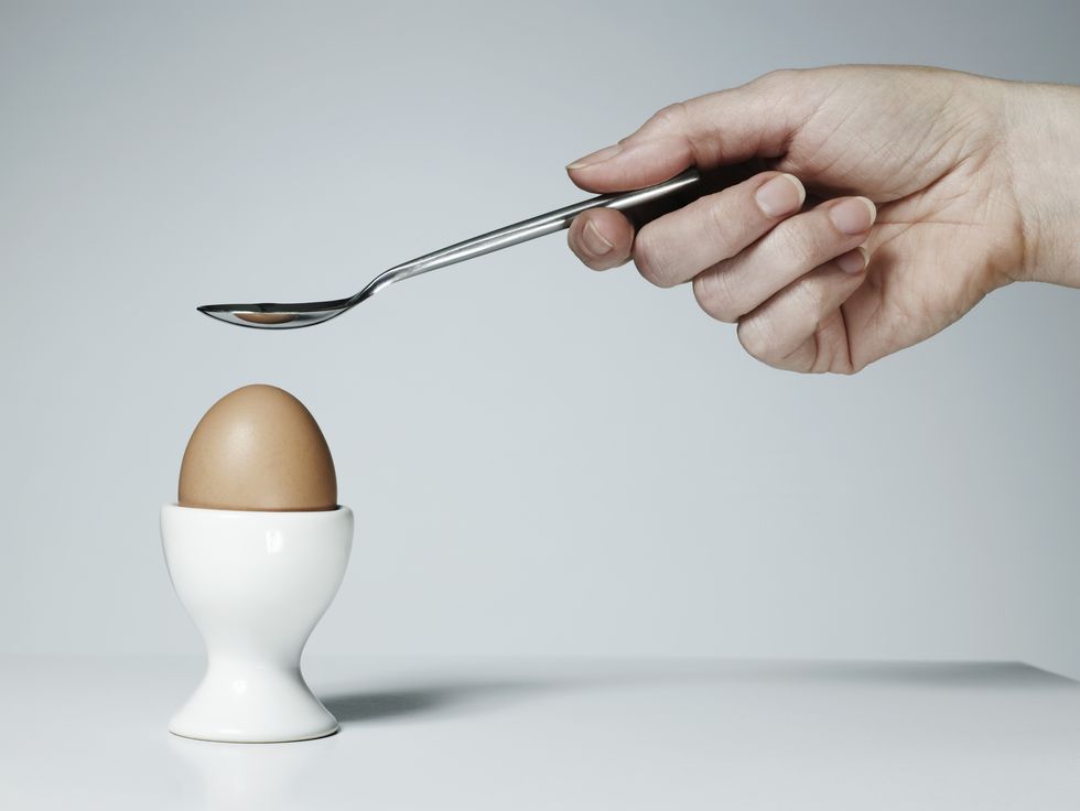 hand with spoon and soft boiled egg