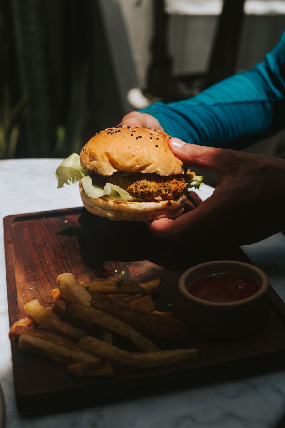 hands holding burger with vegetable cutlet and french fries
