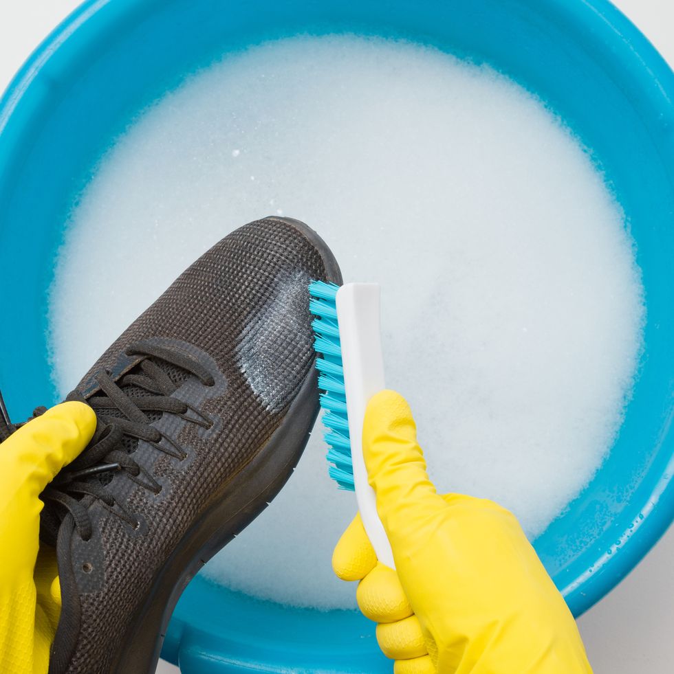 hands in rubber protective gloves holding black sport shoe and brush above blue basin regular care about sneakers washing concept point of view shot closeup top view