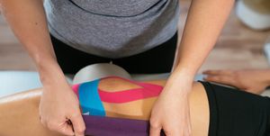 hands of a female physiotherapist taping light blue medical tape over another pink tape on a patient's knee