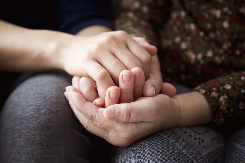 hands of a senior woman and her daughter holding each other's hands together