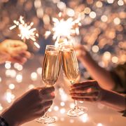 hands of couple with flutes of champagne and their friends with bengal lights