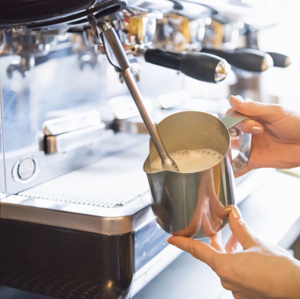 hands of female barista frothing milk with espresso machine in coffee shop