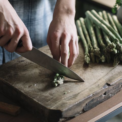 hands of man cutting fresh asparagus on board in kitchen