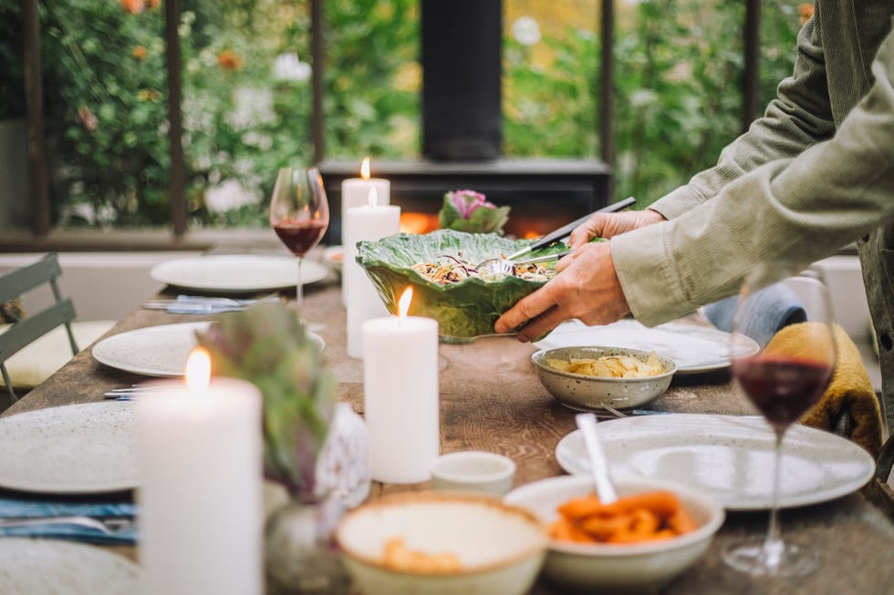 Hands of an elderly man holding a salad bowl while preparing the dining table for a party