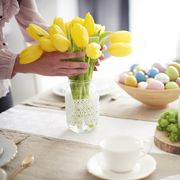 hands of woman arranging yellow tulips at easter dining table