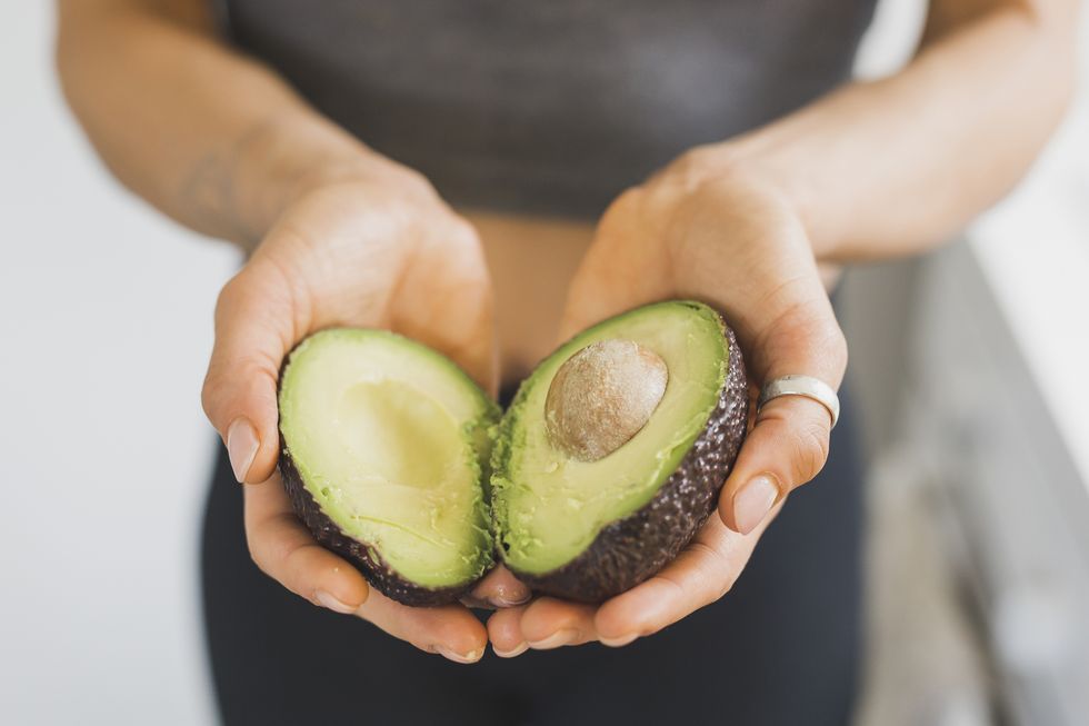 hands of woman holding halved avocado