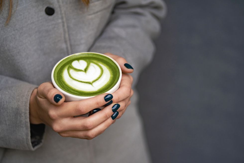 hands of woman in gray coat hold a ceramic cup with matcha green tea latte with foam art backdrop for your design with copy space close up photography from above