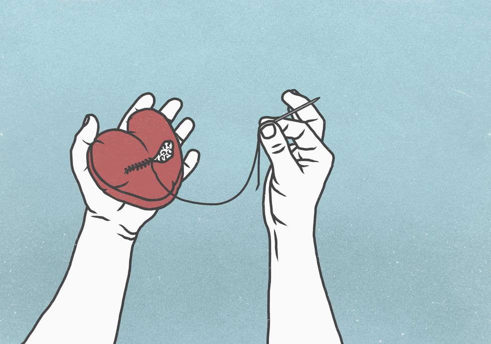 hands sewing broken heart with needle and thread