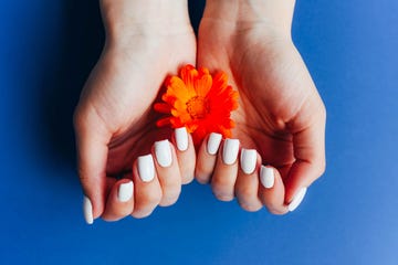 hands with white manicure on a blue background with orange flowers