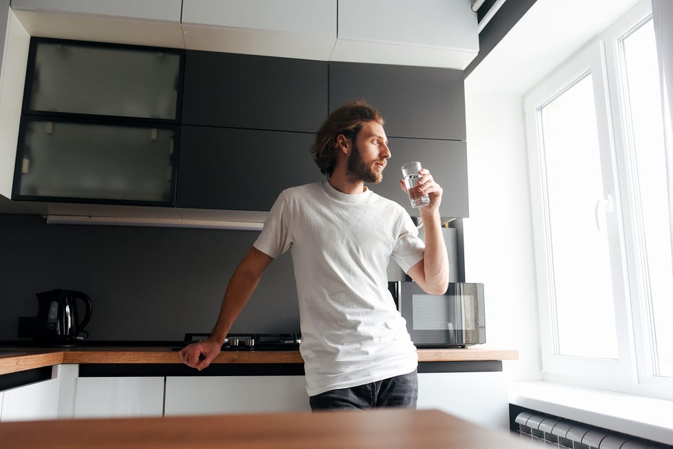a handsome bearded guy stands and drinks water in the kitchen modern cuisine water bearded guy casual style glass of water