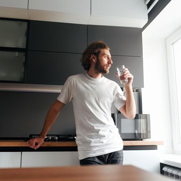 a handsome bearded guy stands and drinks water in the kitchen modern cuisine water bearded guy casual style glass of water