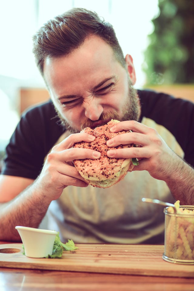 Handsome Male Eating A Cheeseburger In Fast Food Restaurant
