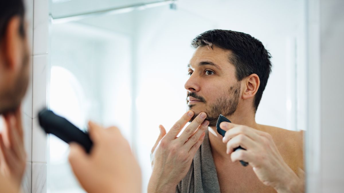 https://hips.hearstapps.com/hmg-prod/images/handsome-man-shaving-his-beard-with-an-electric-royalty-free-image-1681221540.jpg?crop=1xw:0.84335xh;center,top&resize=1200:*