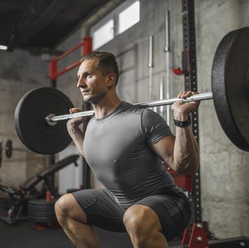 handsome muscular man doing squat exercise with barbell at the gym