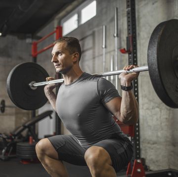 handsome muscular man doing squat exercise with barbell at the gym