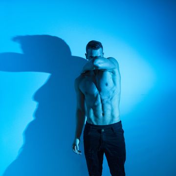 Handsome shirtless man wearing black jeans standing in front of white wall