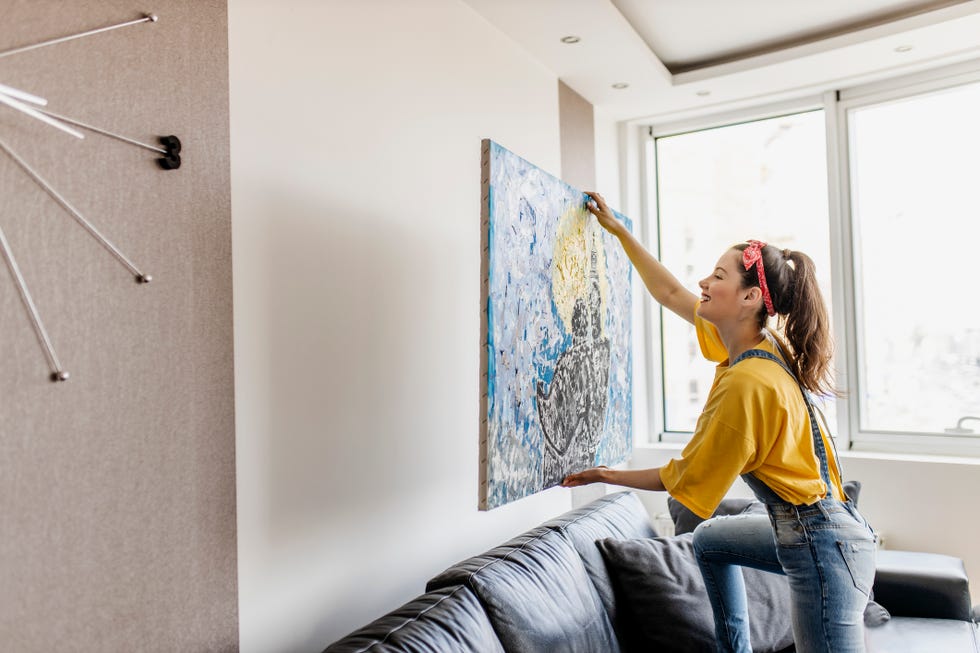 young woman hanging art picture on wall and decorating living room