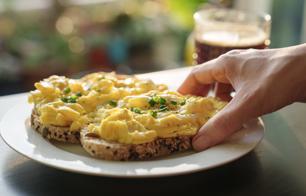 woman reaching for scrambled eggs on toast