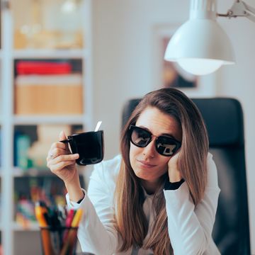 hangover woman drinking coffee wearing sunglasses in the office