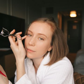 hannah einbinder holding an eyelash curler and compact and gazing at the camera