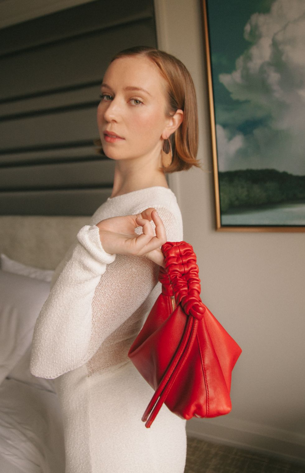 hannah einbinder posing in a white dress with a red purse thrown over her shoulder