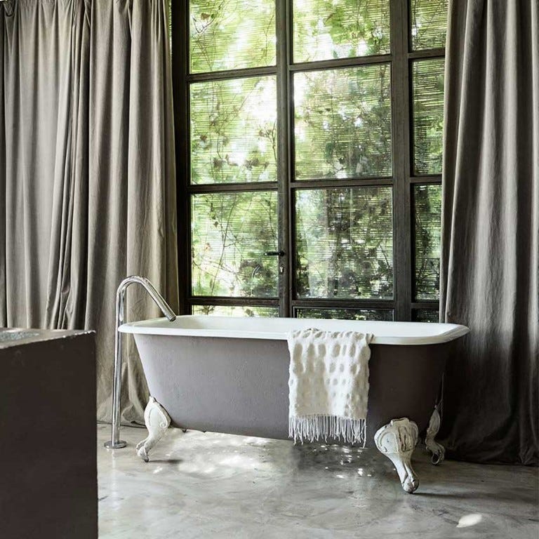 Free standing traditional roll top bath painted grey on concrete floor with grey drapes