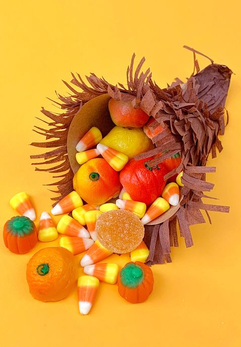 small cornucopia made out of brown fringed paper stuffed with candy corn and candy pumpkins