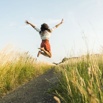 enthusiastic happy young woman jumping high in the air on path through a field