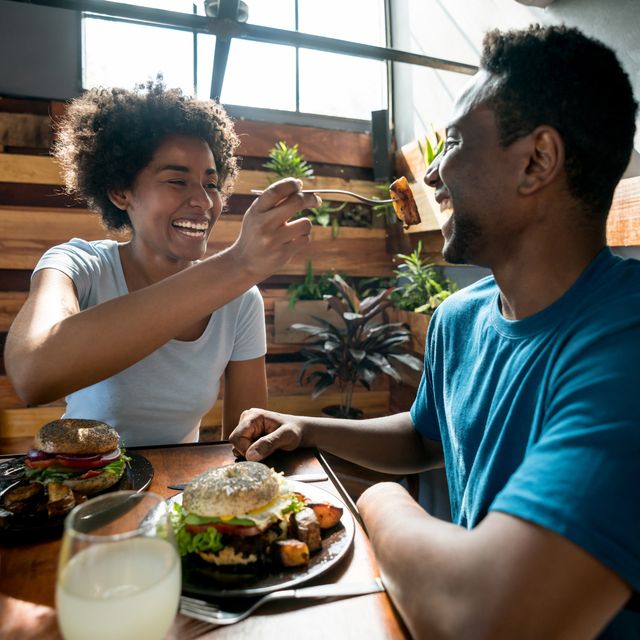 Happy african american couple at a restaurant and woman feeding her boyfriend