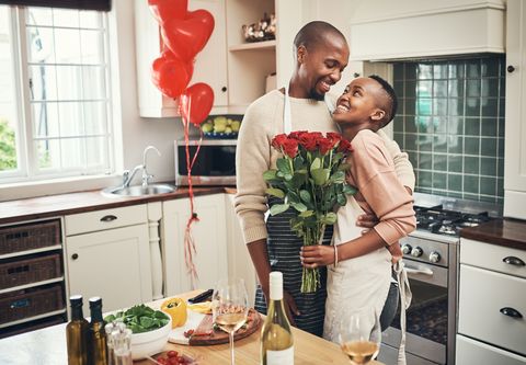 black couple in a kitchen with red balloons, wine, and red roses