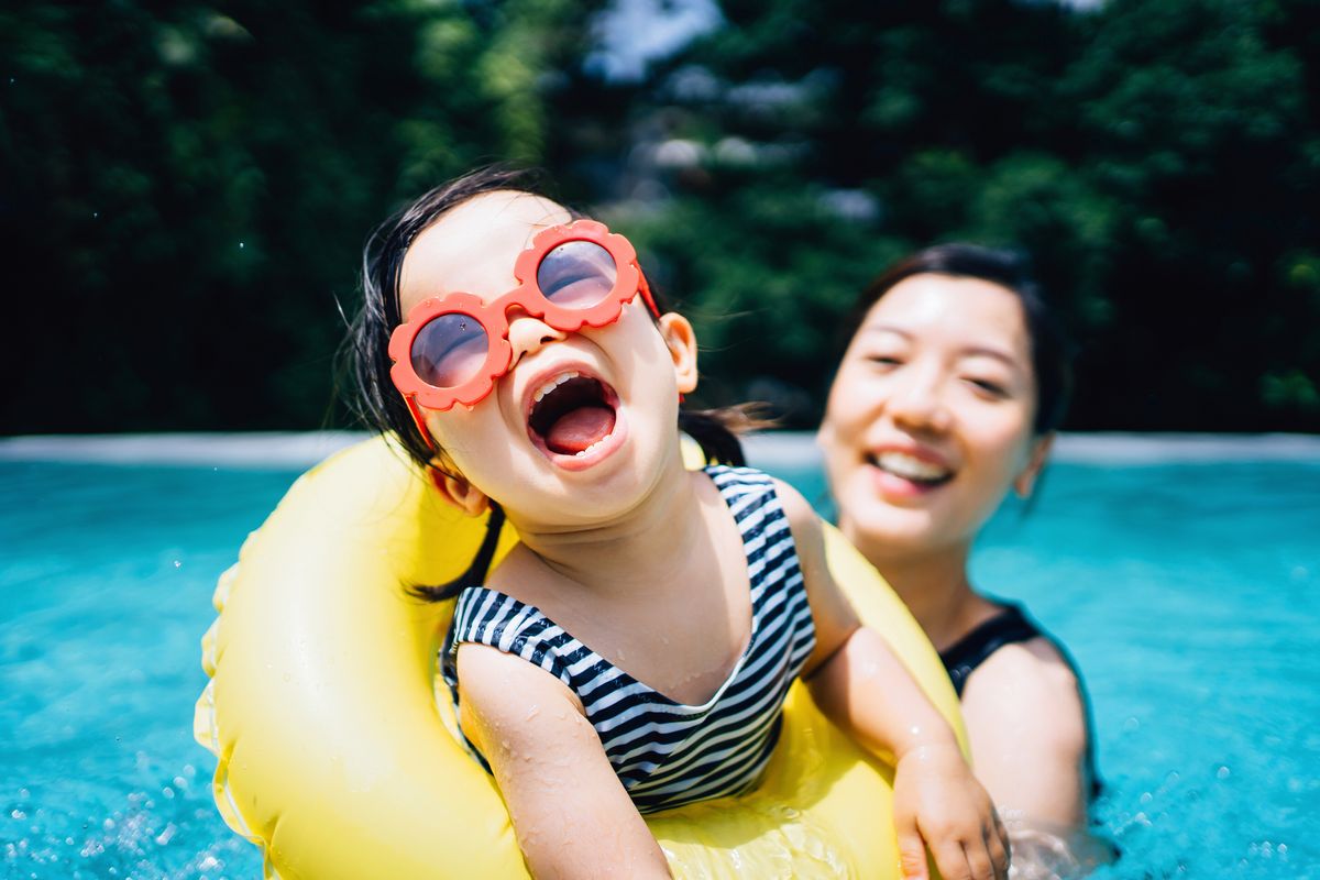 Happy Asian toddler girl with sunglasses smiling joyfully and enjoying family bonding time with mother having fun in the swimming pool in summer