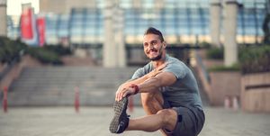 happy athletic man stretching his leg while crouching outdoors