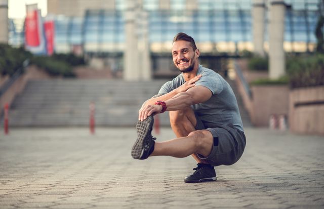 happy athletic man stretching his leg while crouching outdoors