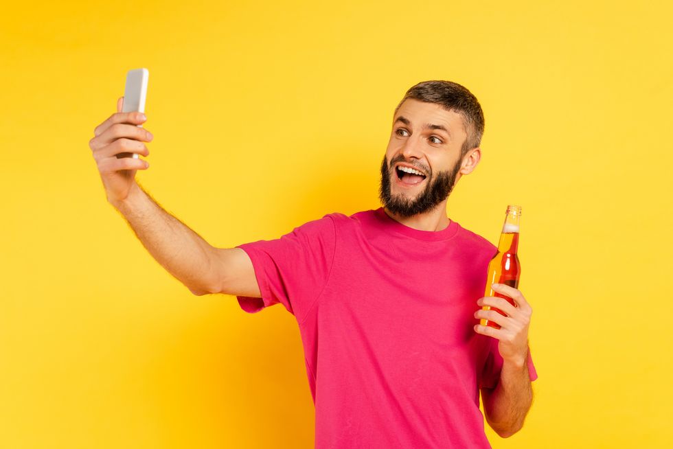 happy bearded guy in pink t shirt taking selfie with beer on yellow