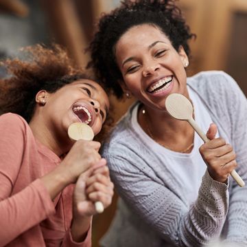 happy mother and daughter singing with wooden spoons at home