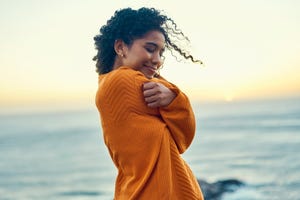 happy woman embrace herself on a beach at sunrise, self love and peaceful young african american feeling in touch with earth and nature, enjoy freedom and inner peace, smiling, loving soul