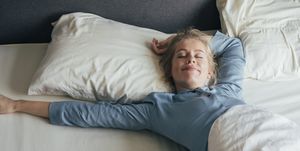 happy blonde woman in pyjamas stretches in bed after waking up in the morning