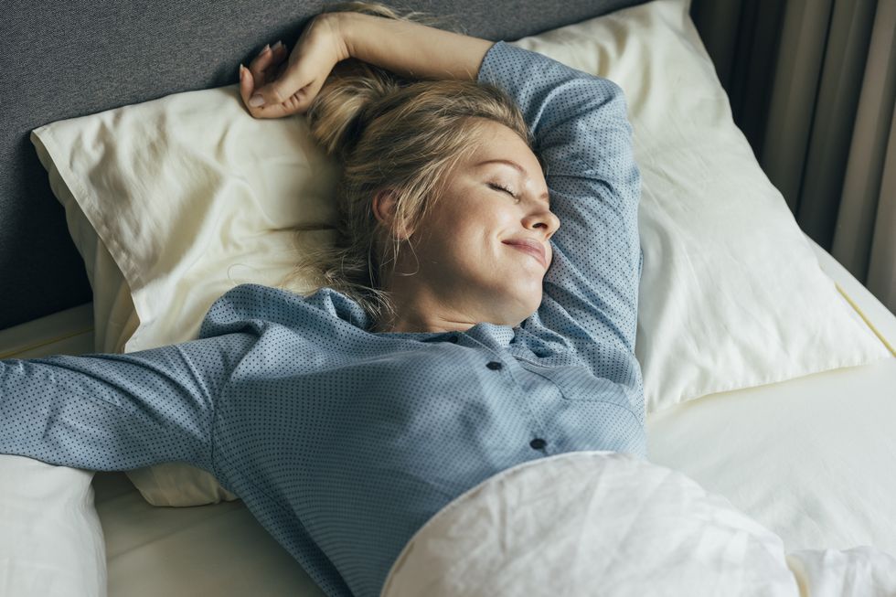 feeling energized happy blonde woman in pyjamas stretches in bed after waking up