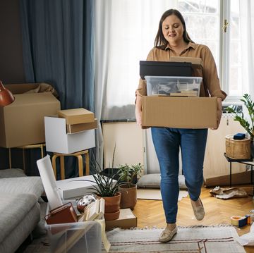 ready to move out happy caucasian plus size woman standing in the middle of a messy room while holding boxes with personal belongings