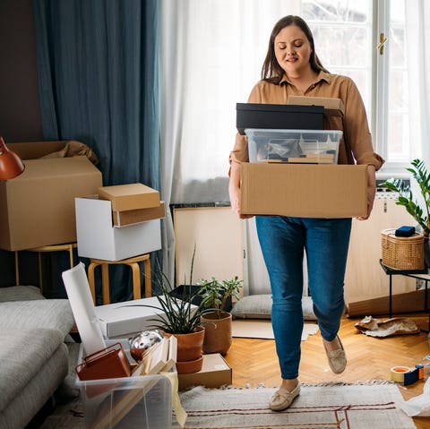 ready to move out happy caucasian plus size woman standing in the middle of a messy room while holding boxes with personal belongings