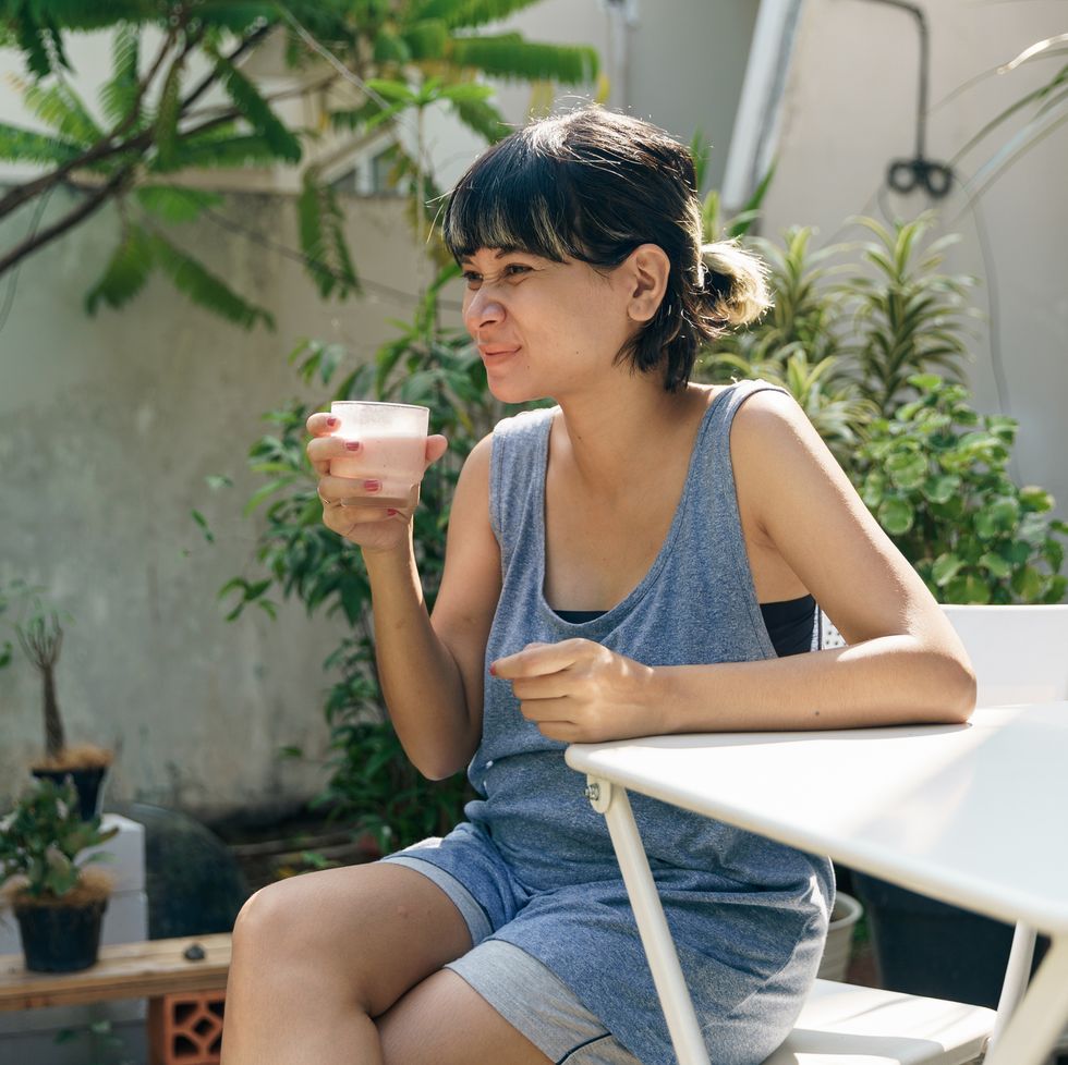 happy confident asian woman drinking smoothie in the garden at home. short highlighted hair