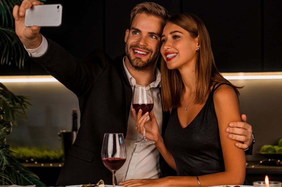 Happy couple having dinner and taking selfie using smartphone indoors