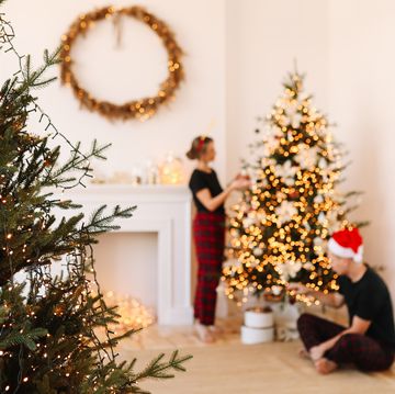 a happy couple in love in pajamas are preparing for the holiday, celebrating christmas and new year by decorating a christmas tree in the cozy interior of the house in winter in december
