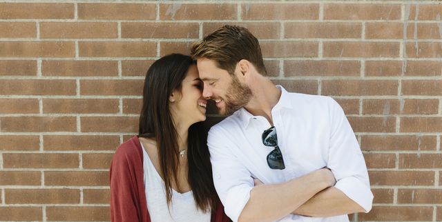 Happy couple standing in front of brick wall, kissing
