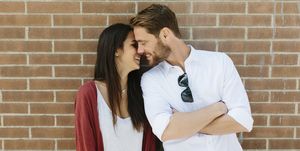 Happy couple standing in front of brick wall, kissing