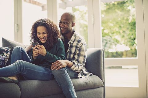 happy couple using smart phone on sofa at home